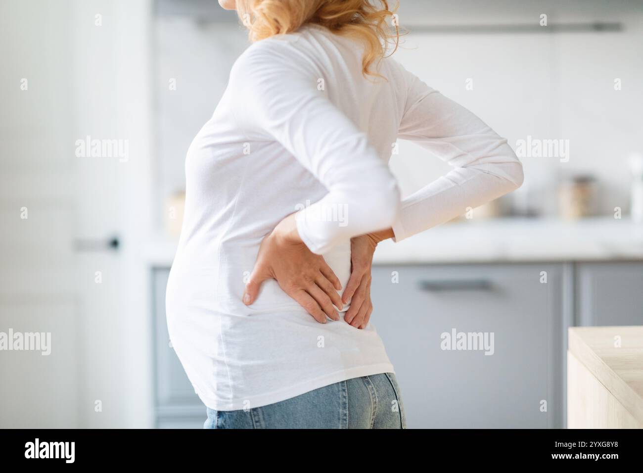 Pregnant woman experiencing back pain in modern kitchen during morning ...