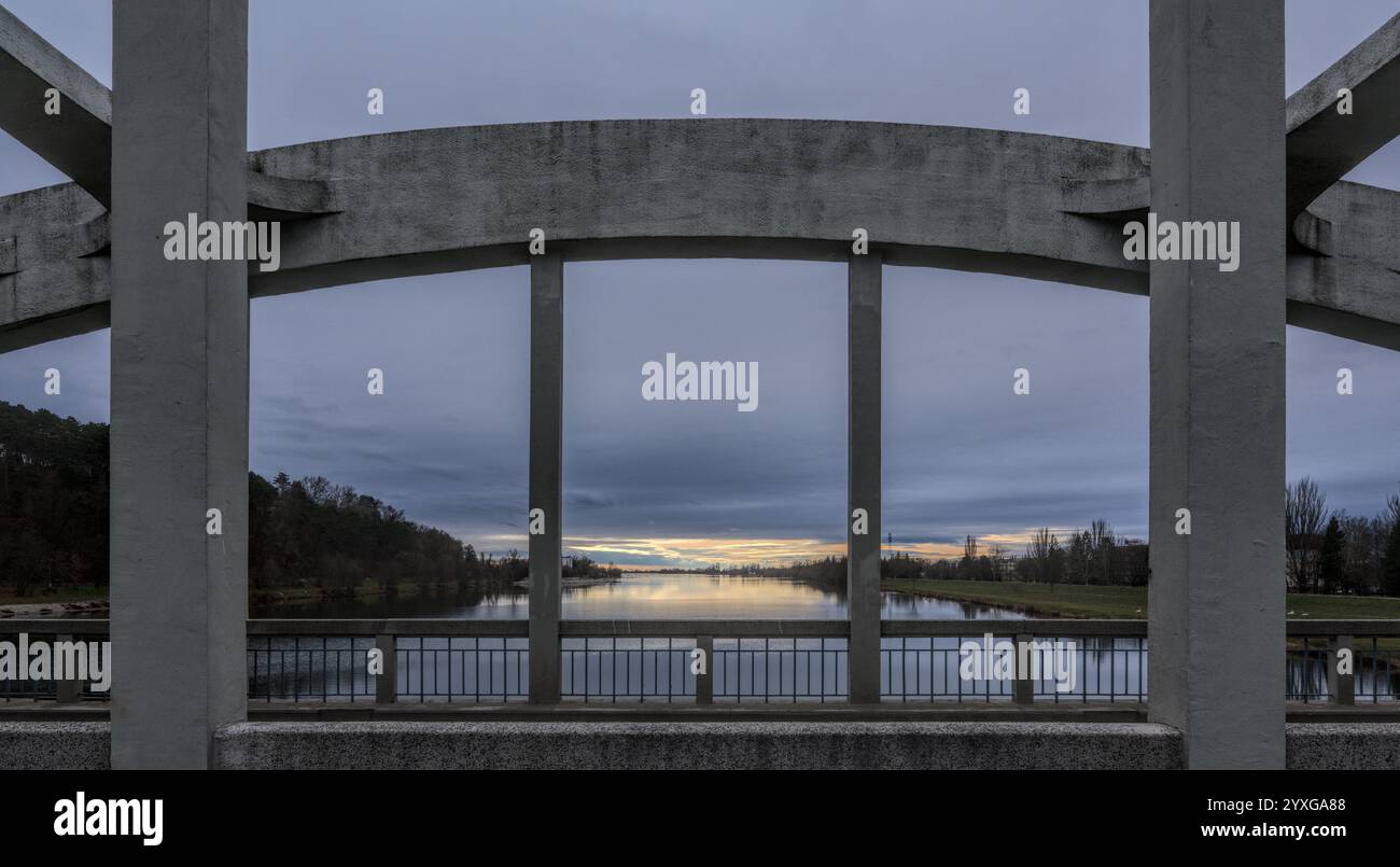 A concrete bridge arch framing a calm river, with a view of the sunset ...
