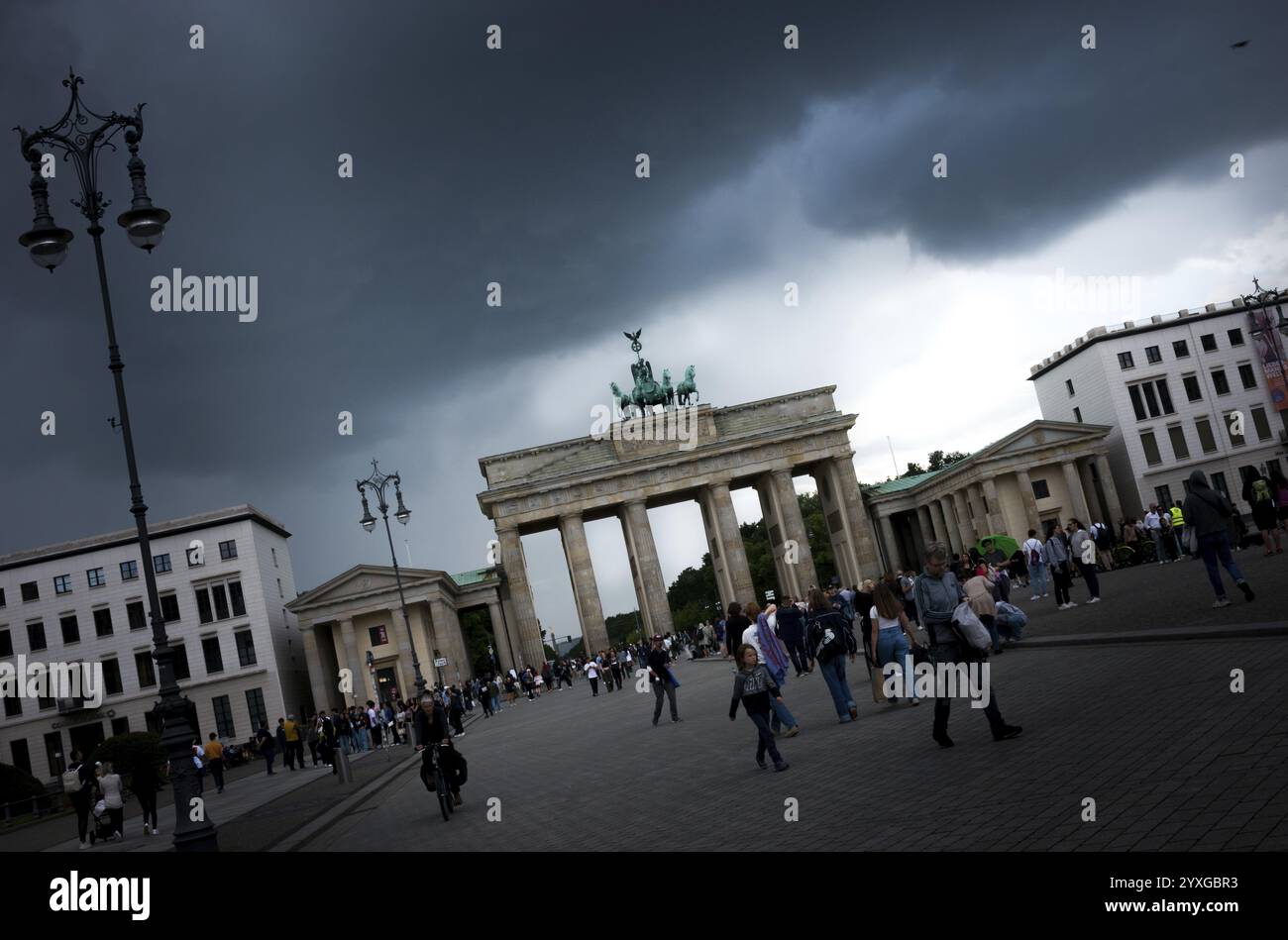 People visit the Brandenburg Gate on a day with a threatening, dramatic sky and heavy clouds, a crow (Corvus corone) flies into the picture, light shi Stock Photo