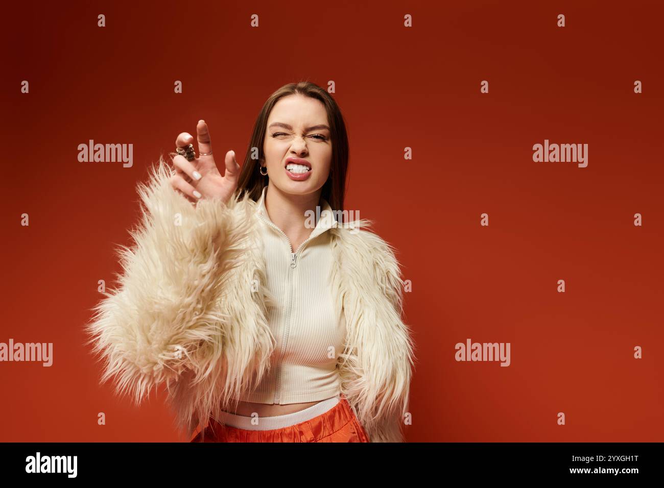 A vibrant woman in a fluffy jacket playfully poses with a cheeky expression in a bold setting. Stock Photo