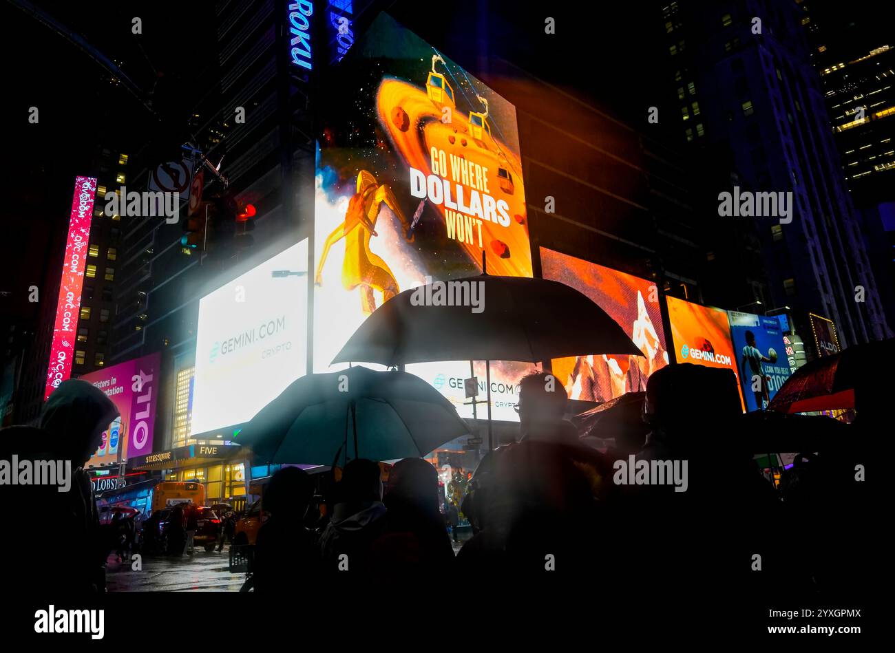 Crowds of people pass under an advertisement for the Winklevoss brothers' Gemini Cryptocurrency Exchange in the rain in Times Square in New York on Wednesday, December 11, 2024. Twins Cameron and Tyler Winklevoss founded the exchange in 2014 trading Bitcoin and other cryptocurrencies.  (© Richard B. Levine) Stock Photo