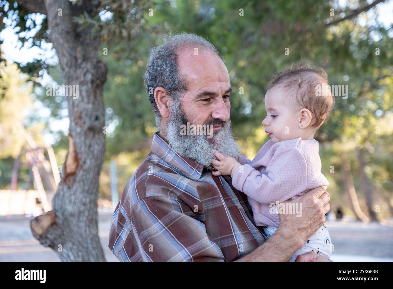 A touching moment captured between grandfather and grandchild sharing a gentle embrace in nature's golden light, showcasing the beautiful bond between Stock Photo