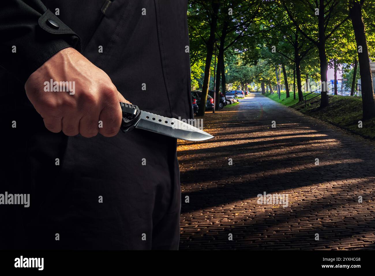 Criminal holding a knife closeup view, city park street background ...