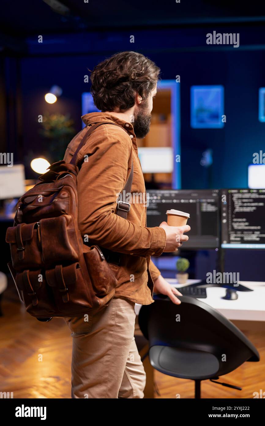 Programmer with disposable cup of coffee entering office to implement security measures, protecting company systems and data. IT worker starting job shift, testing and debugging code Stock Photo