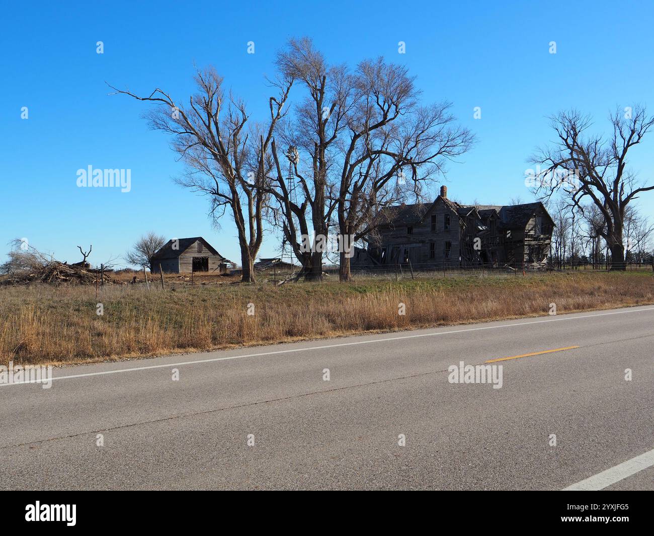 A large, abandoned farmhouse collapsing with age, surrounded by the golden grasslands of the Flint Hills in central Kansas during autumn Stock Photo