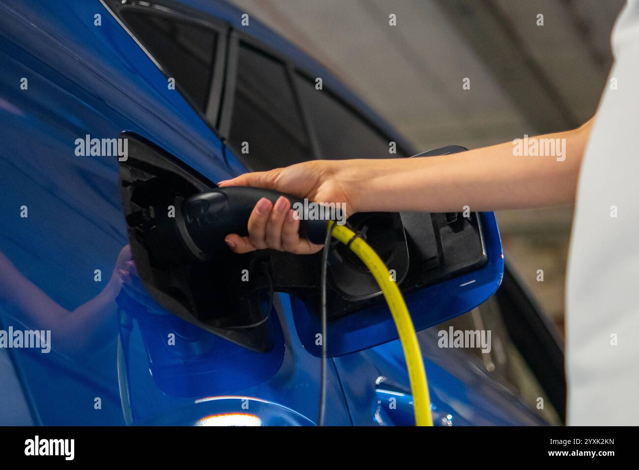Woman hand connects a charger to an electric car, ensuring it is powered up for the journey ahead Stock Photo