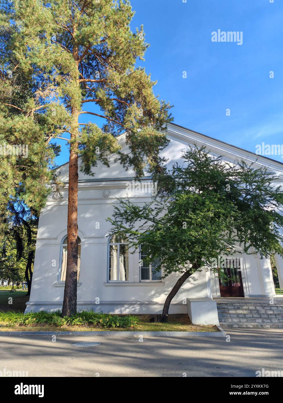 A white neoclassical building surrounded by lush trees and a clear blue ...