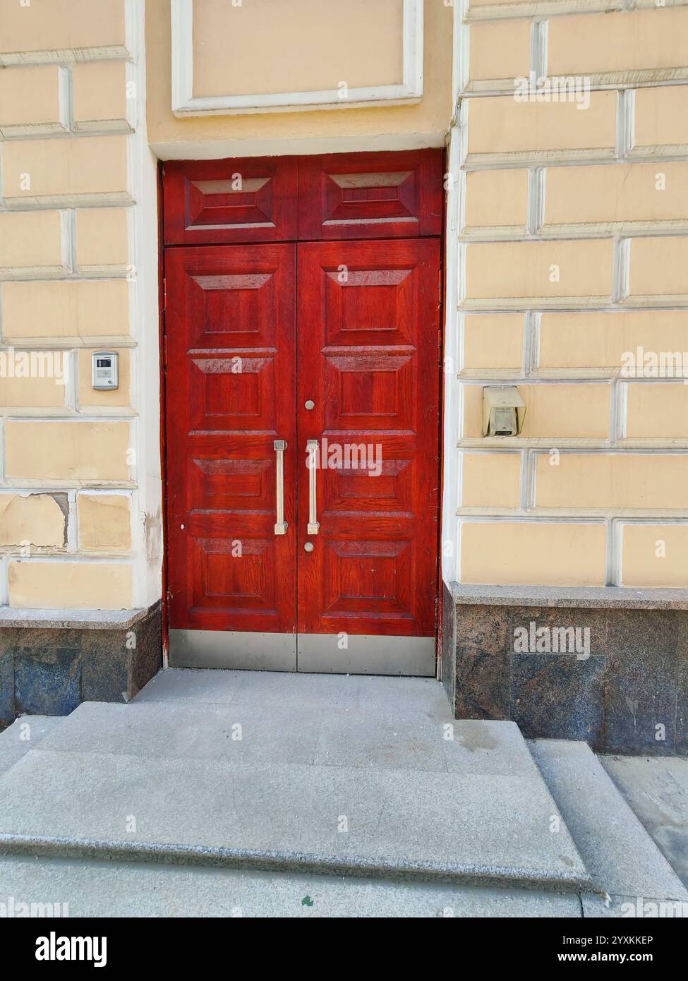 A polished red wooden door leading to an unknown interior, surrounded by aged stone. Doors represent psychological metaphors for transition, mystery Stock Photo