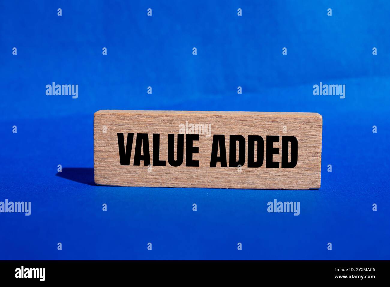 Value added message written on wooden block with blue background ...