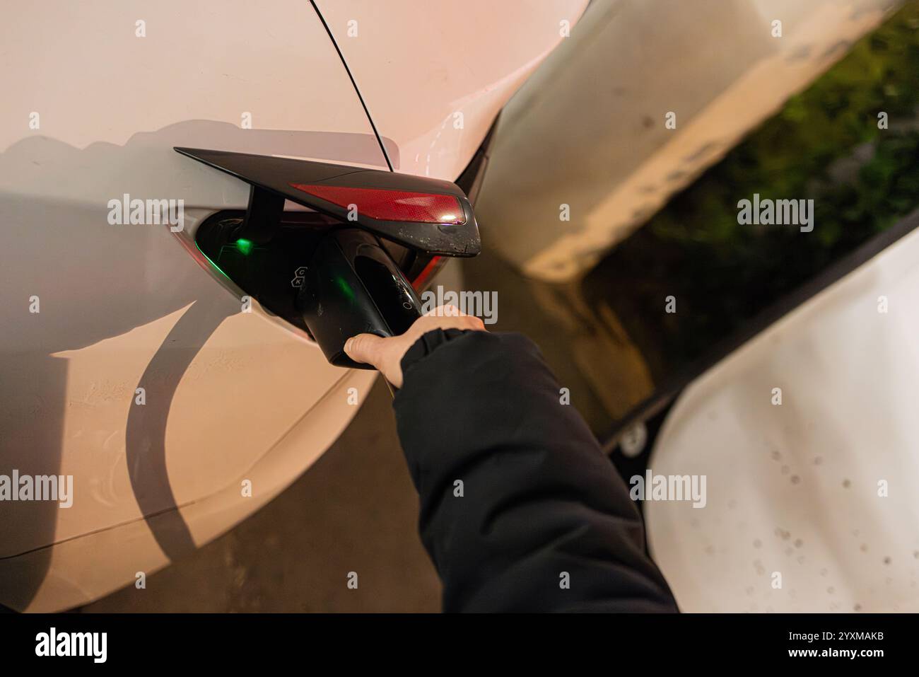 Close-up of an electric vehicle being charged at a modern charging station during nighttime. Stock Photo