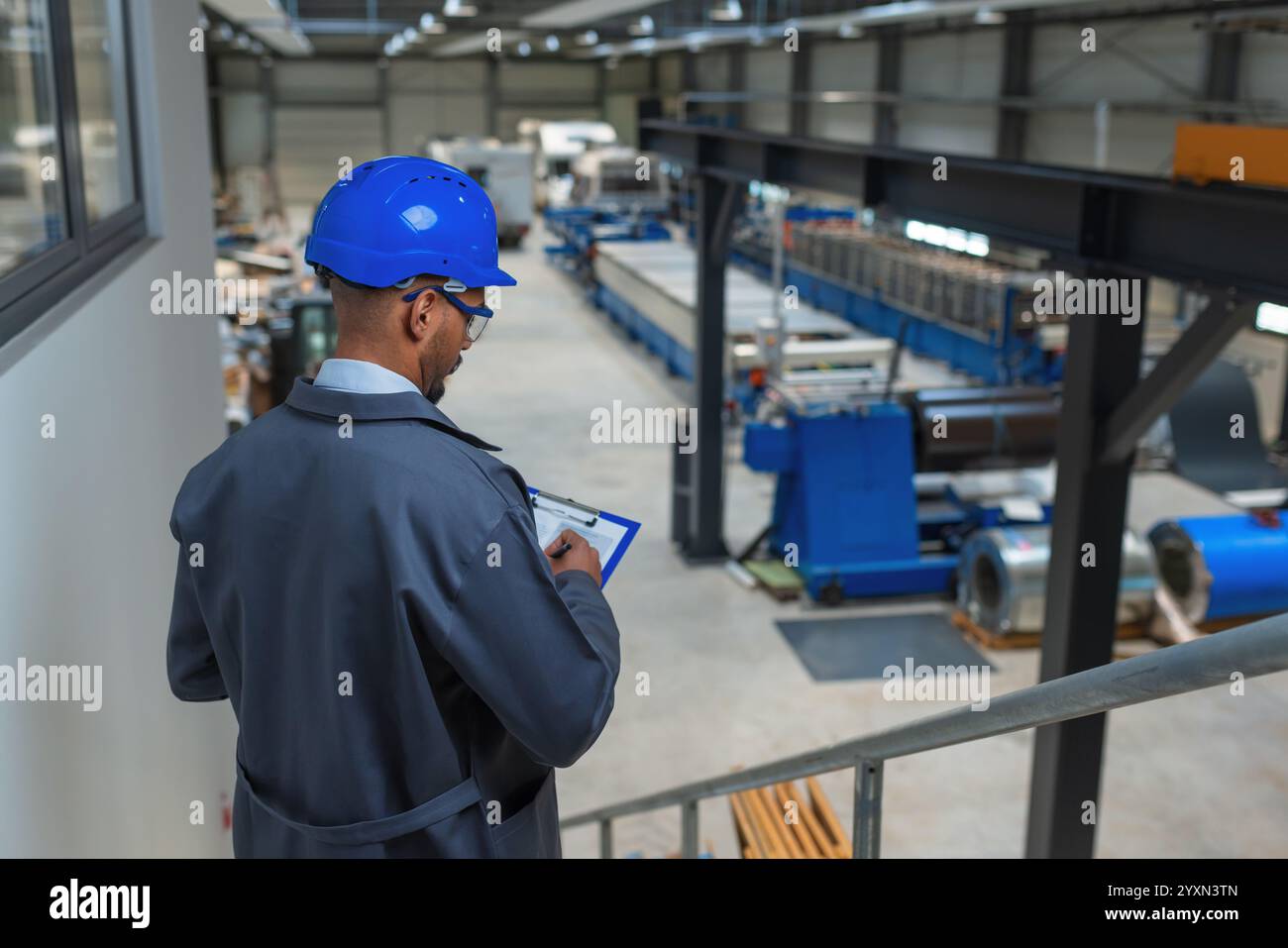 Young engineer programmer using tablet and graphs data to check factory machinery production and work procedure, rear view. Industry career concept. Stock Photo
