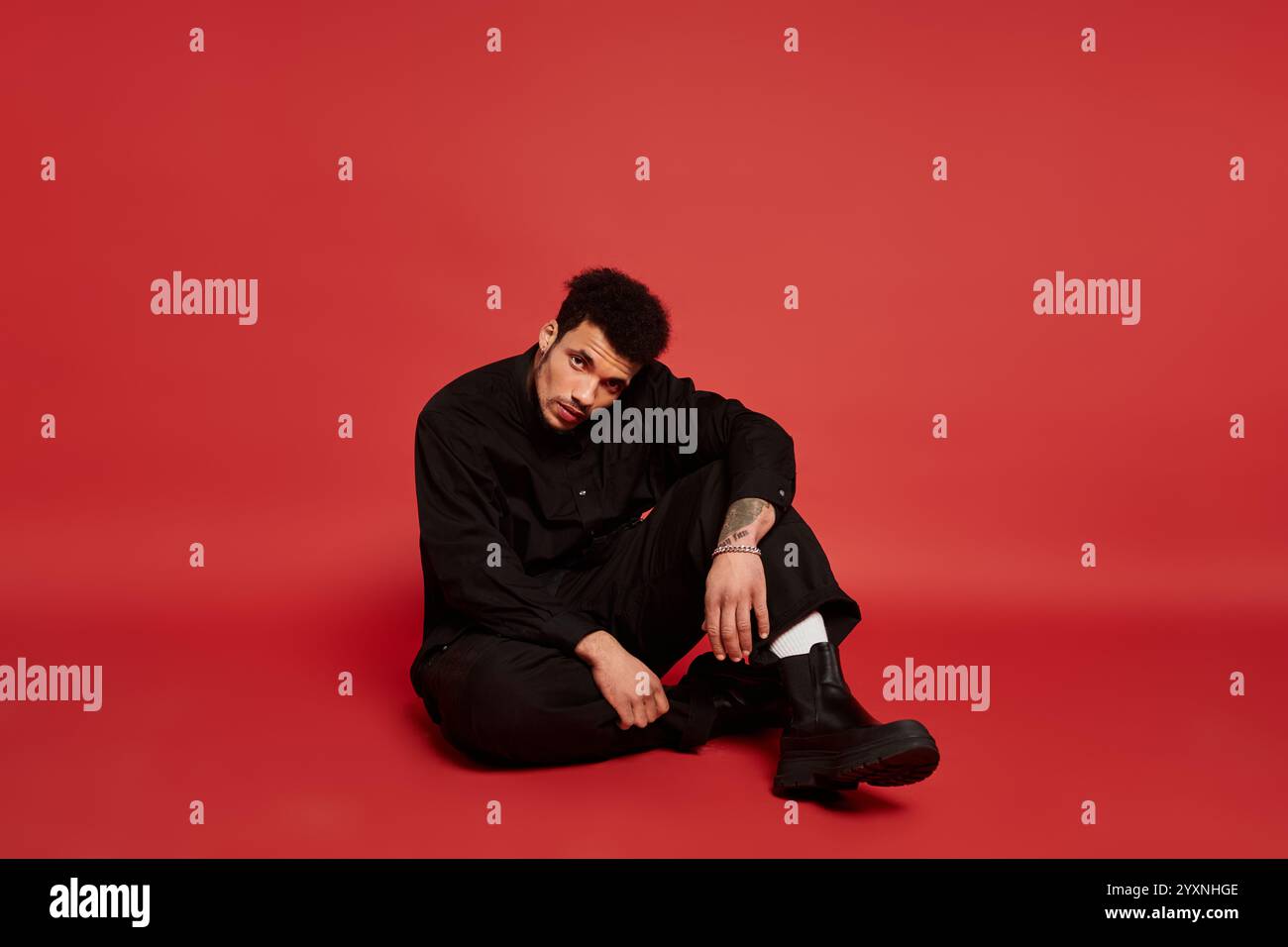 A stylish young man is seated against a bold red backdrop, exuding a ...