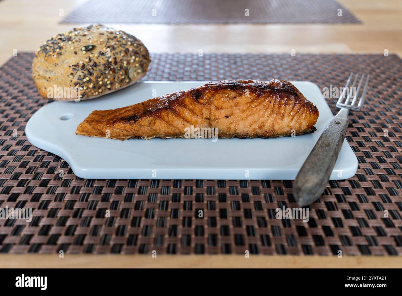 flame-grilled salmon fillet with bread roll on ceramic board on table Stock Photo