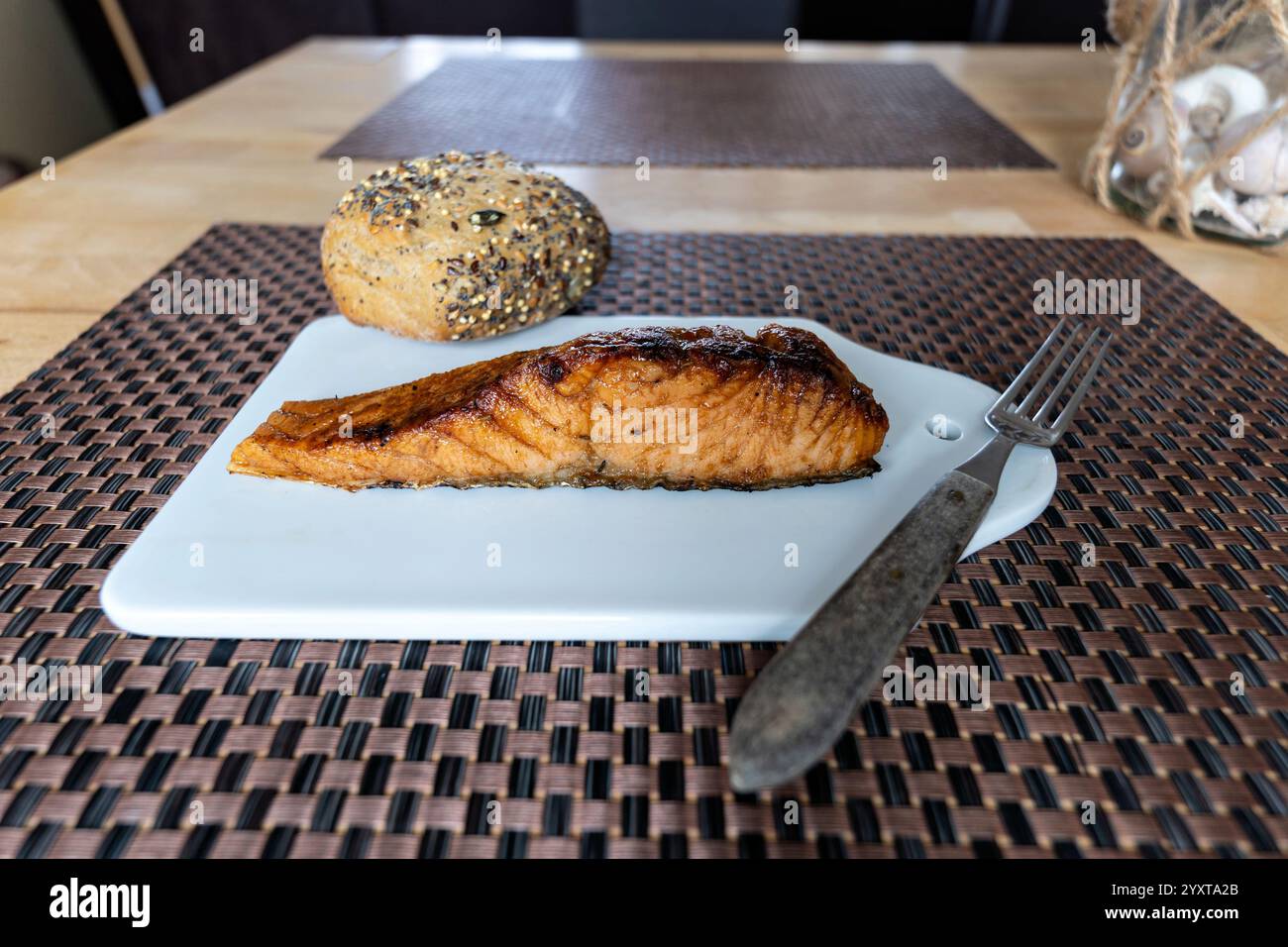 flame-grilled salmon fillet with bread roll on ceramic board on table Stock Photo