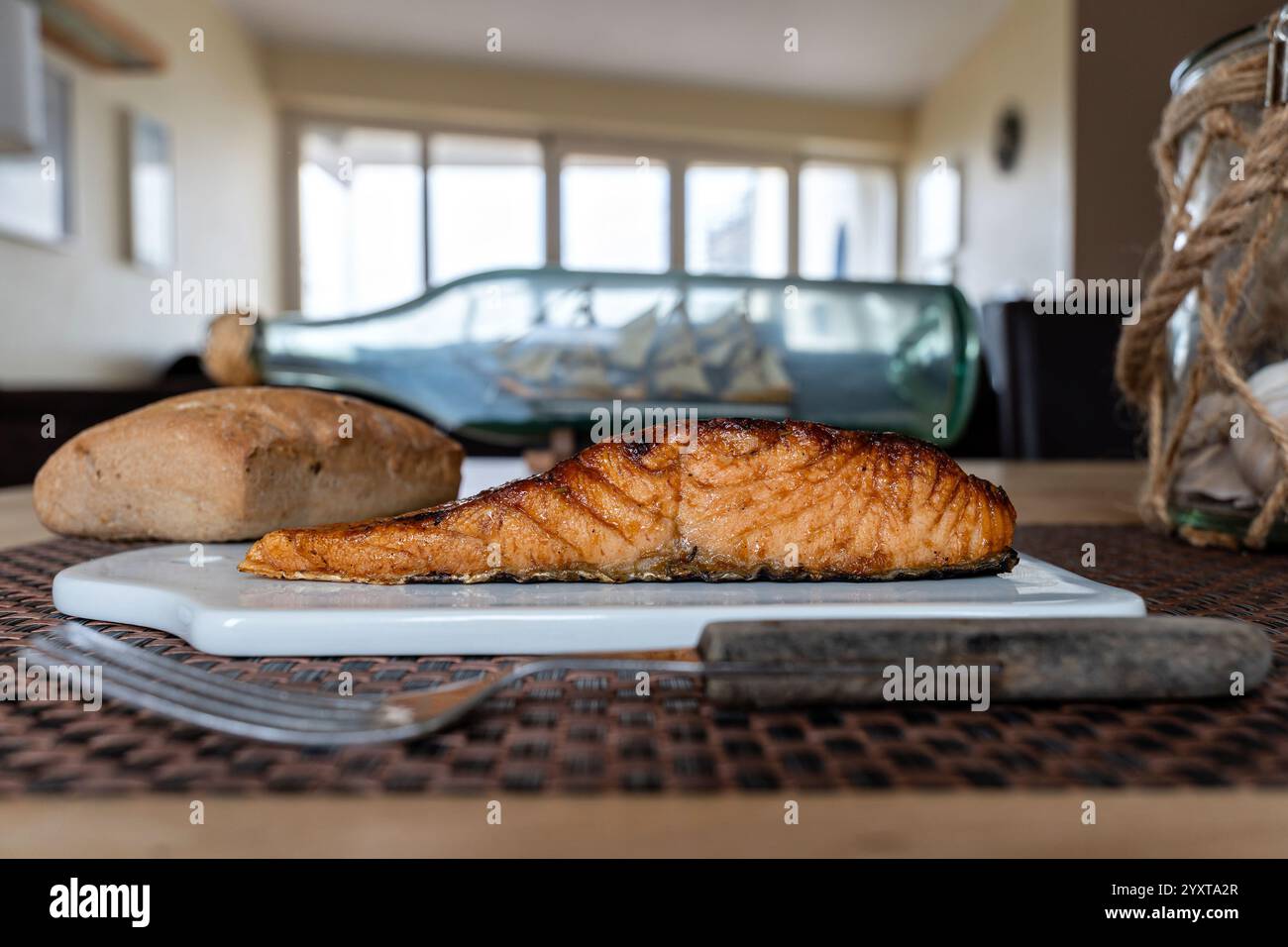 flame-grilled salmon fillet with bread roll on ceramic board on table Stock Photo