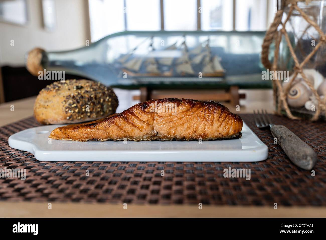 flame-grilled salmon fillet with bread roll on ceramic board on table Stock Photo