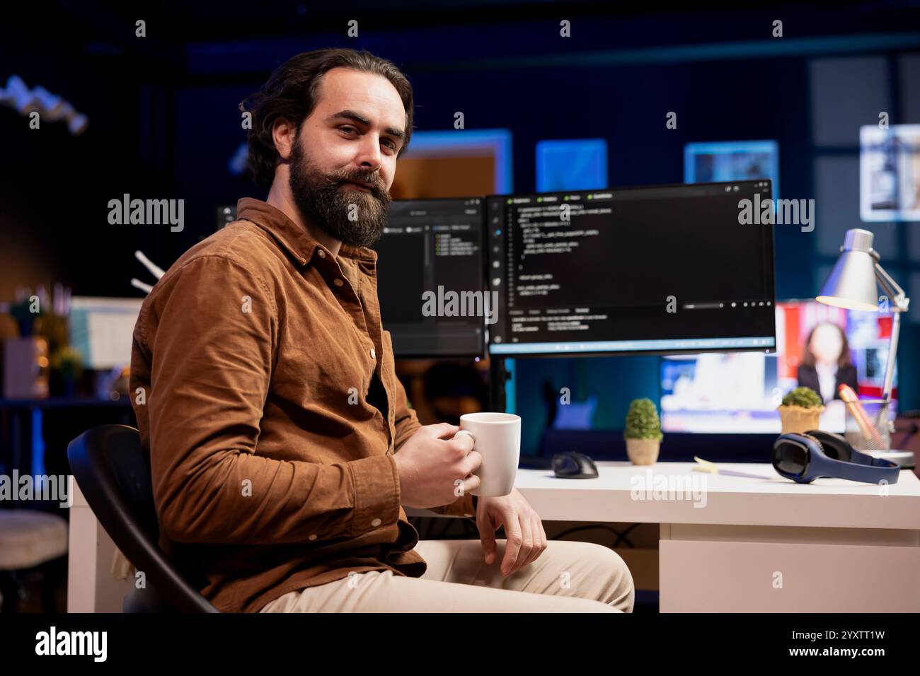 Portrait of cheerful computer engineer enjoying hot beverage while implementing security measures to protect company systems and data. Smiling IT worker drinking coffee and debugging code Stock Photo