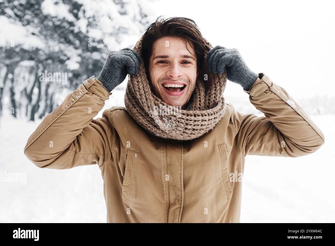 Handsome Man Pulling Scarf On Head Standing In Snowy Forest Stock Photo