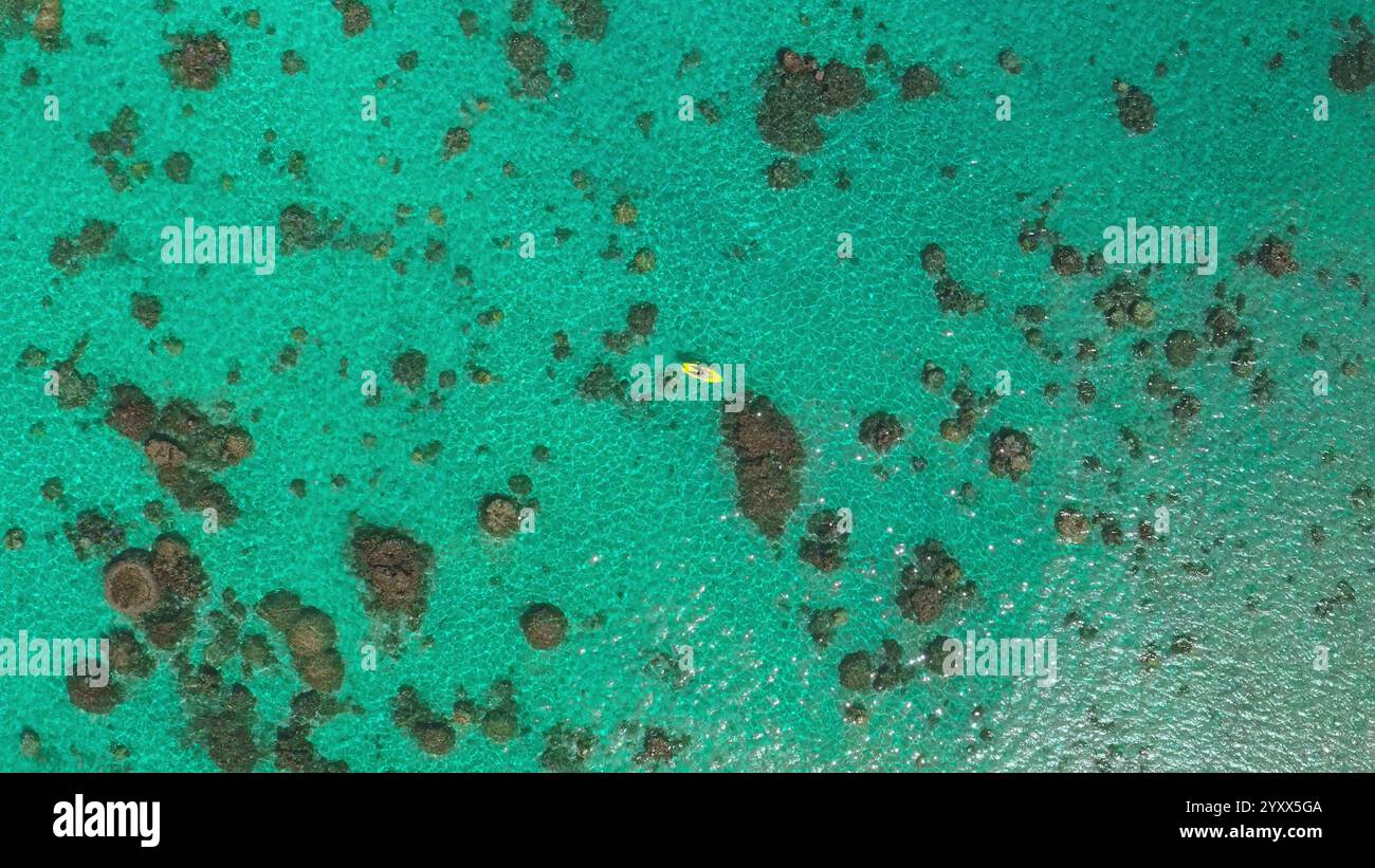 Aerial view of a kayaker paddling a yellow kayak in shallow turquoise ...