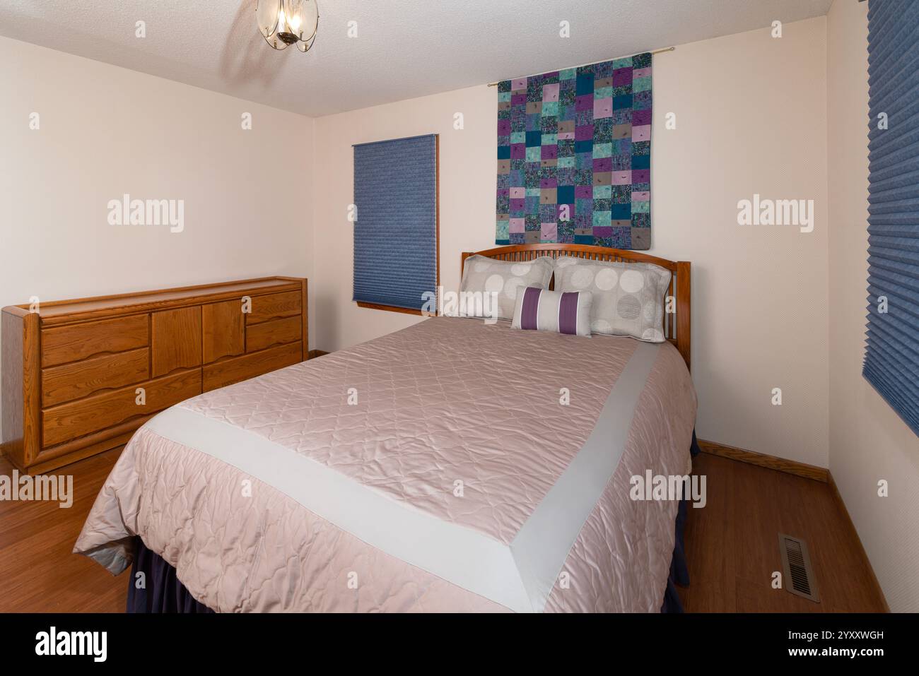 interior of bedroom with queen size bed atop hardwood bamboo floors and decor hanging on wall above bed Stock Photo