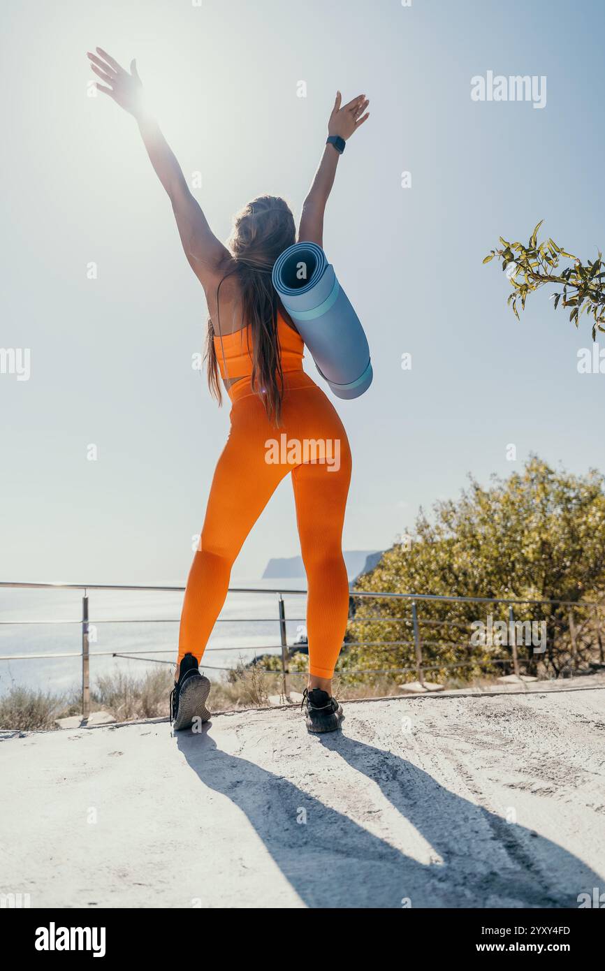 Woman in Orange Sportswear Celebrating on a Clifftop Stock Photo