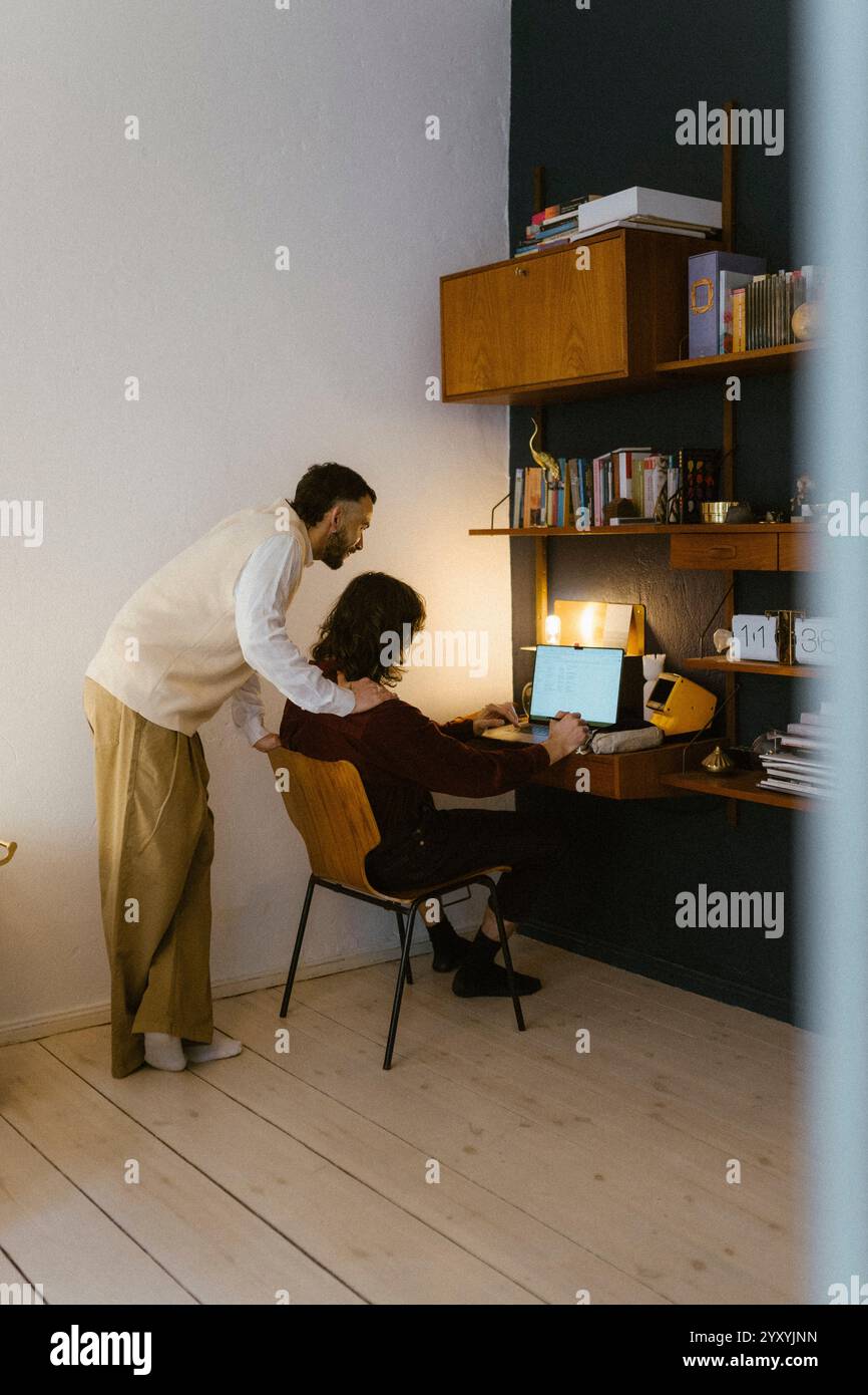 Young man with hand on shoulder of boyfriend using laptop at home Stock Photo