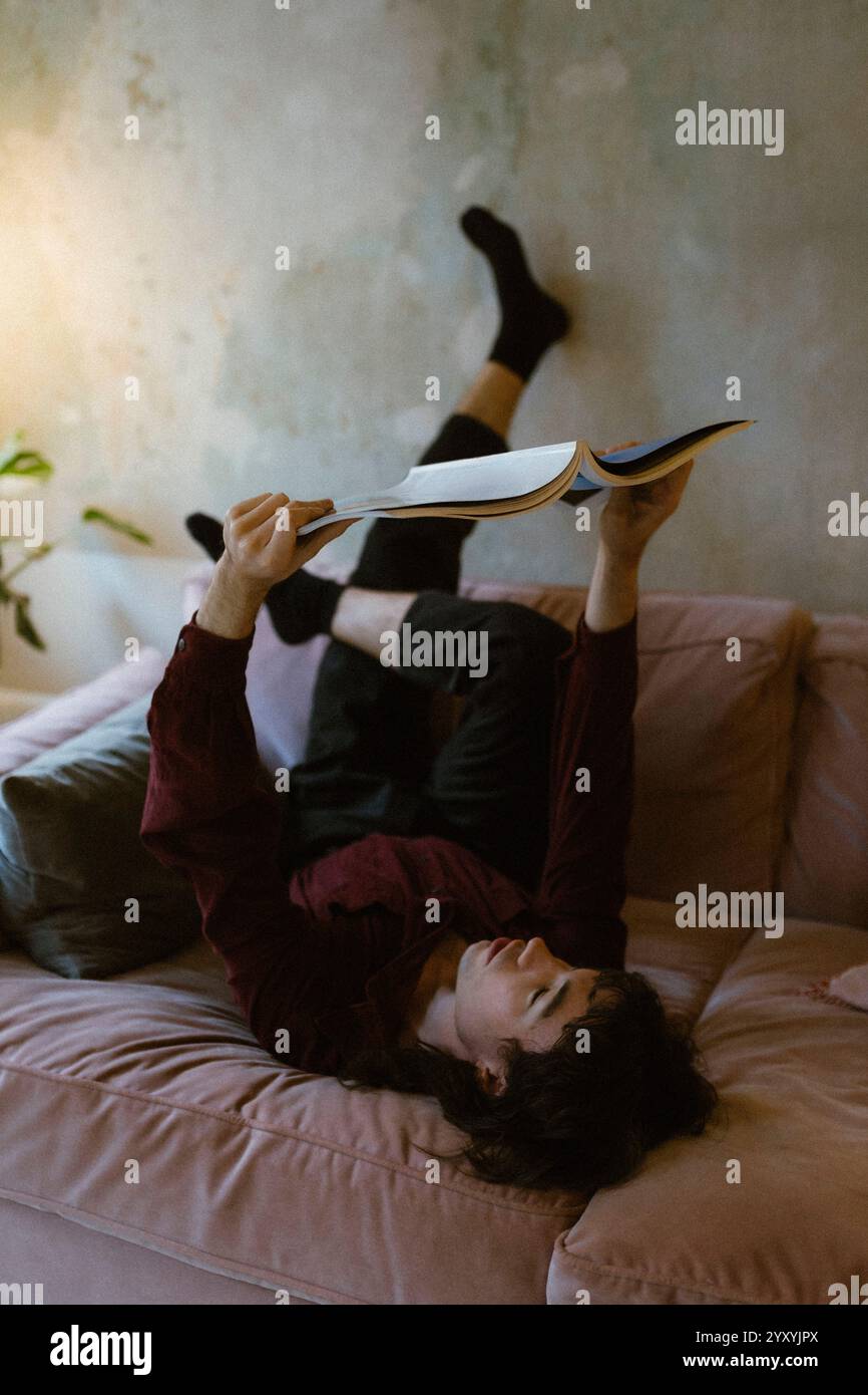 Comfortable young man reading magazine while lying down on sofa at home Stock Photo