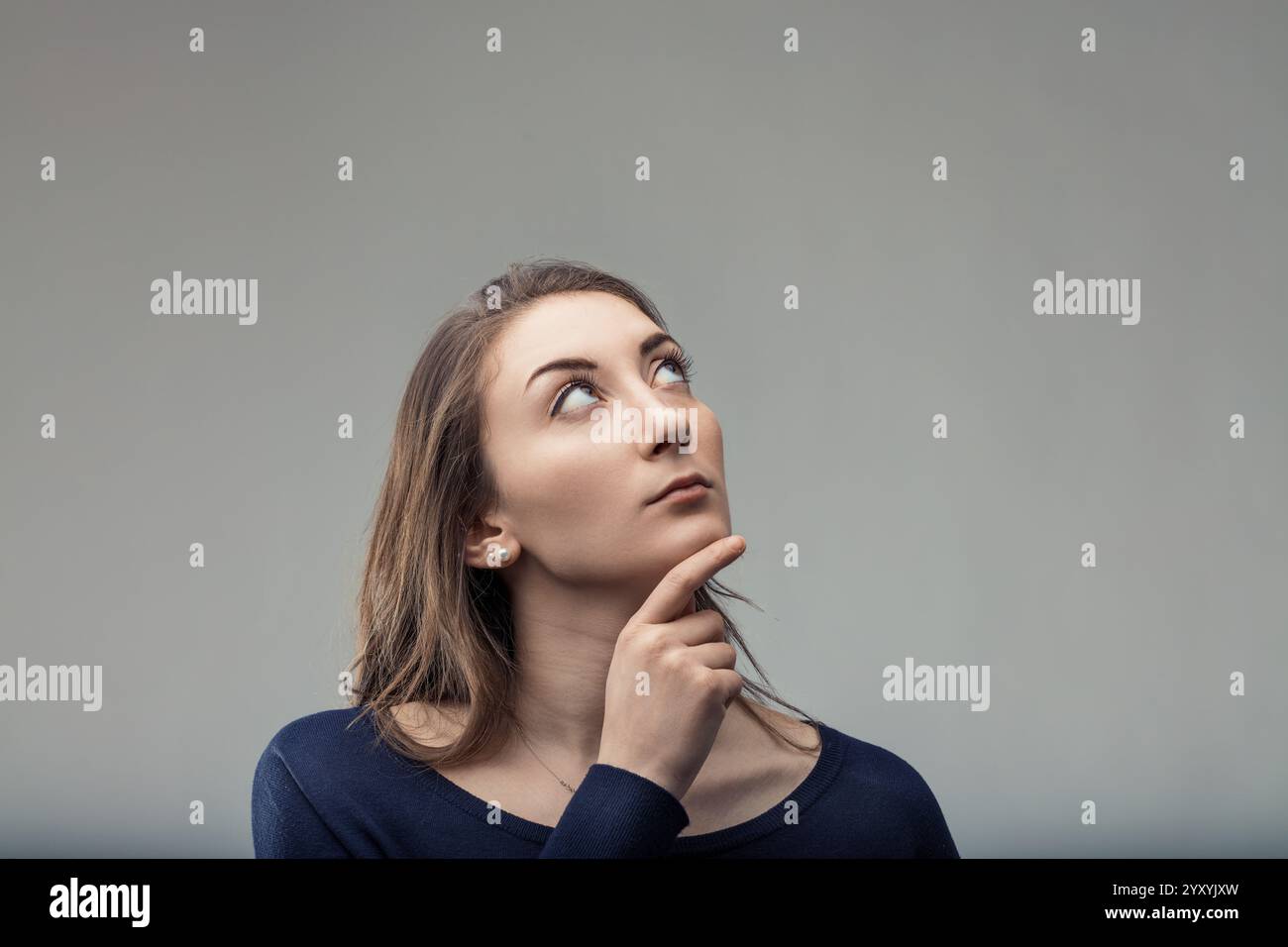Young woman with long brown hair is thoughtfully looking up with her ...