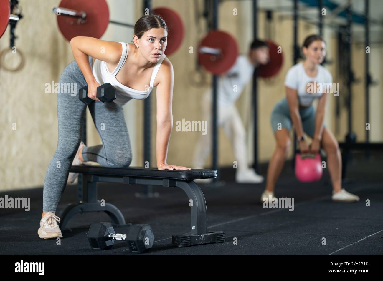 Athletic young woman pumping her biceps with a dumbbell while leaning ...