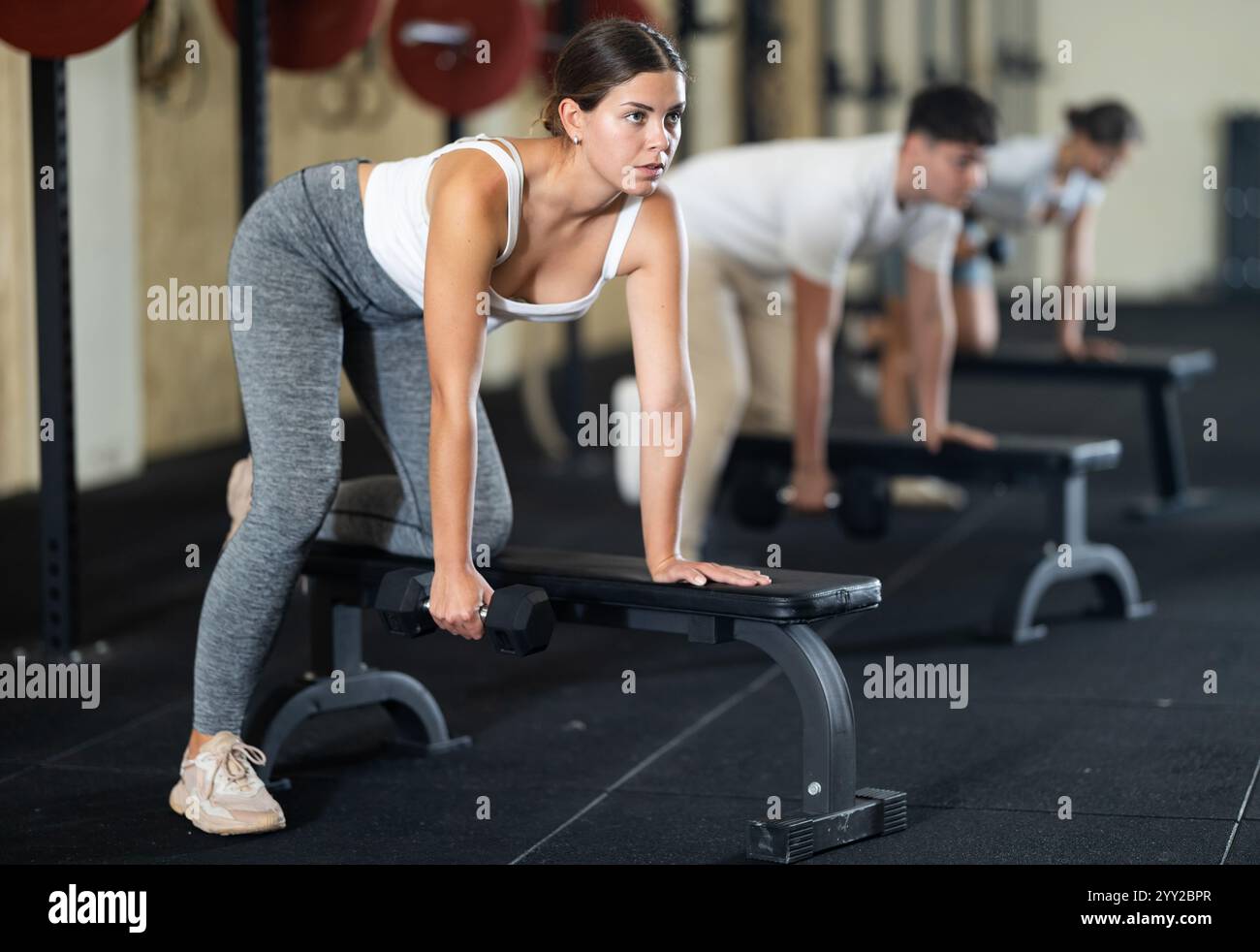 Athletic young woman pumping her biceps with a dumbbell while leaning ...