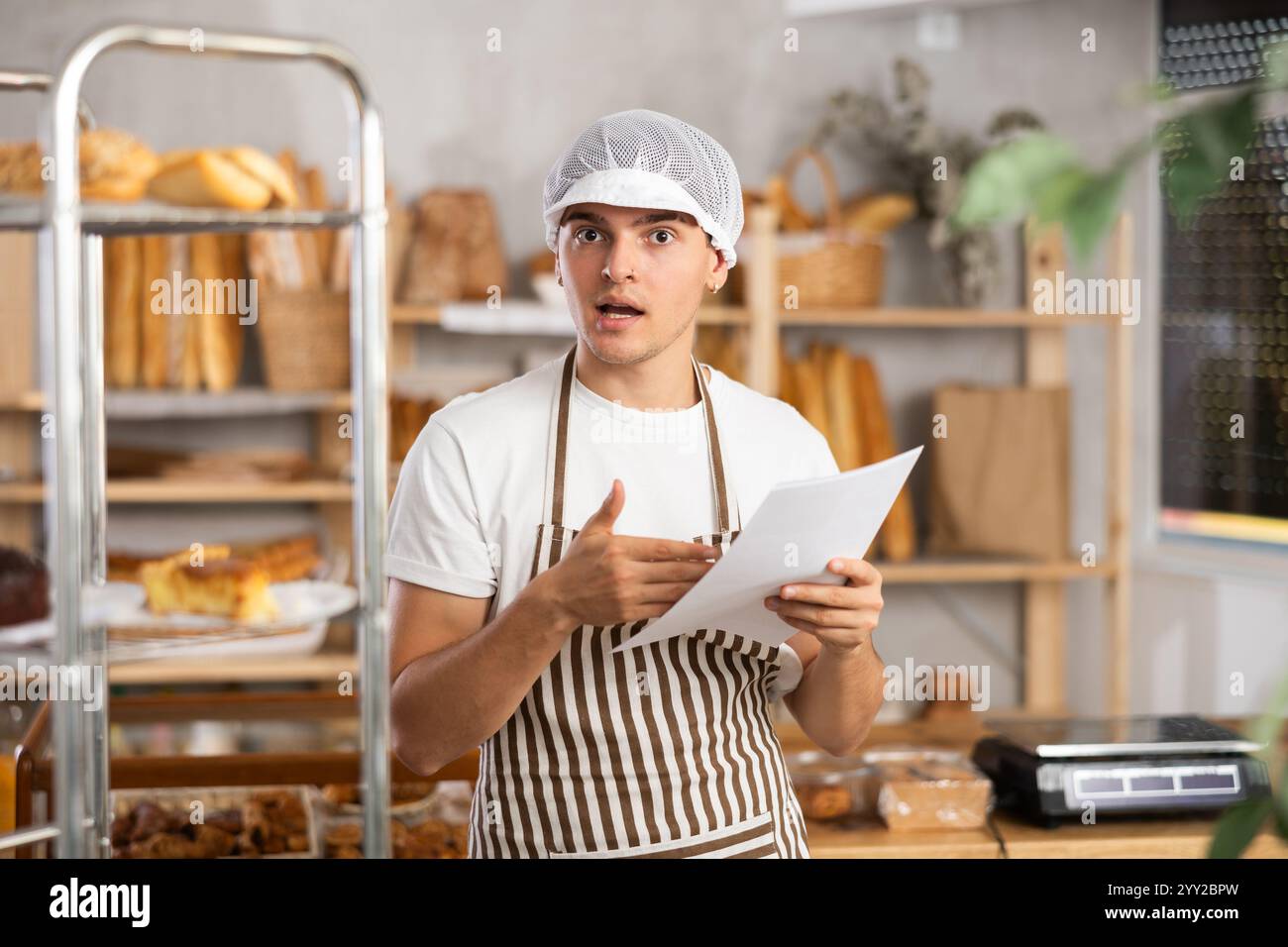 Young baker looking confused while reviewing order documents Stock Photo