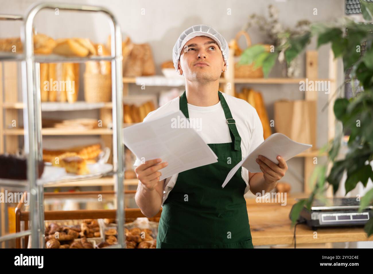 Young baker carefully reads documents and makes calculations in his ...