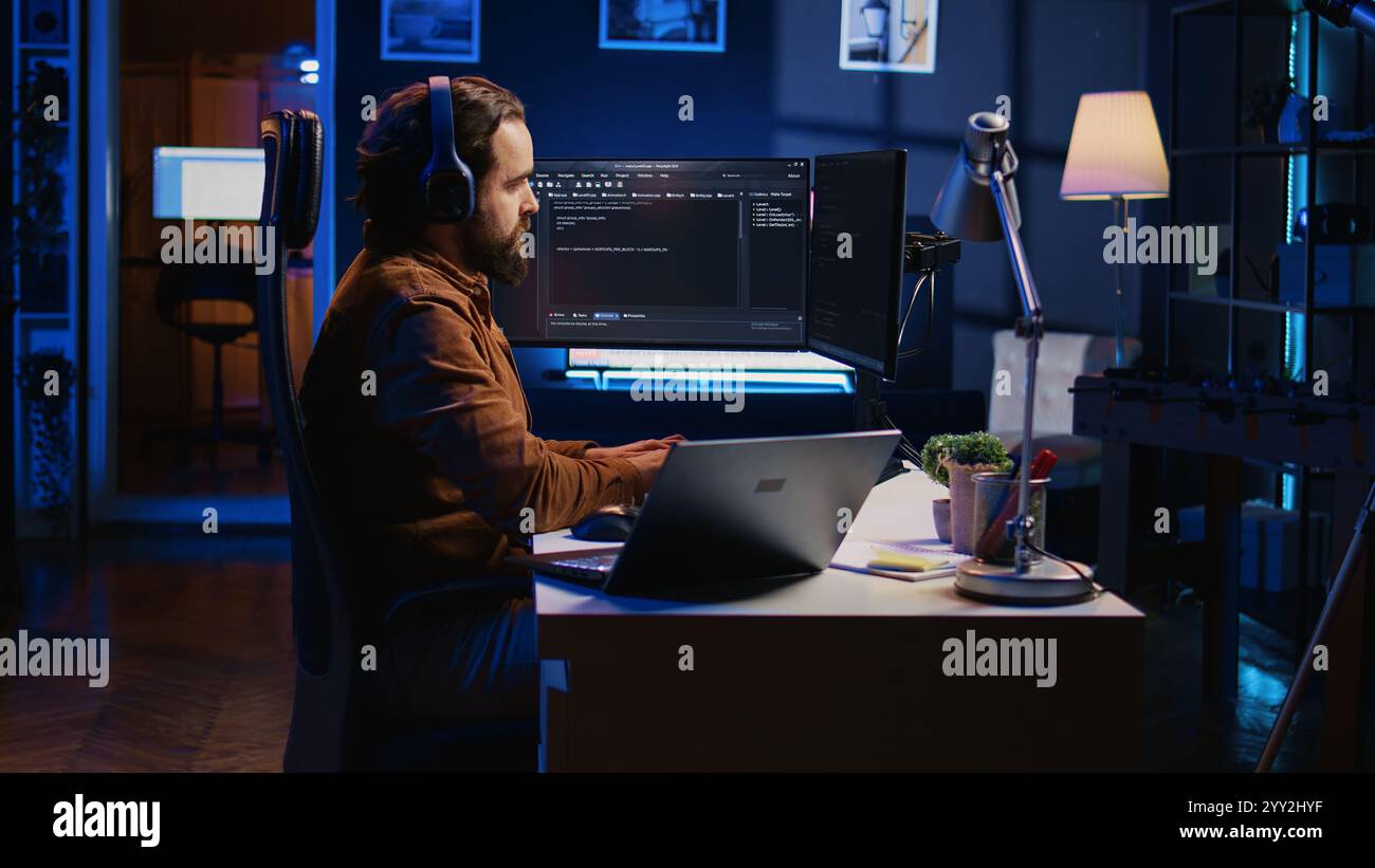 Developer focused on typing complex code in neon lit home office, listening music and developing software application. IT expert wearing headphones, solving coding project tasks on laptop, camera B Stock Photo