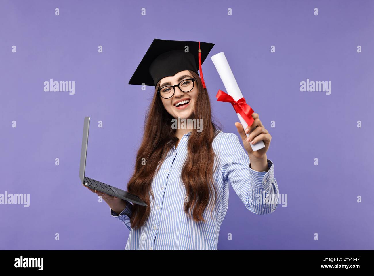 Happy student with laptop and diploma after graduation on violet ...