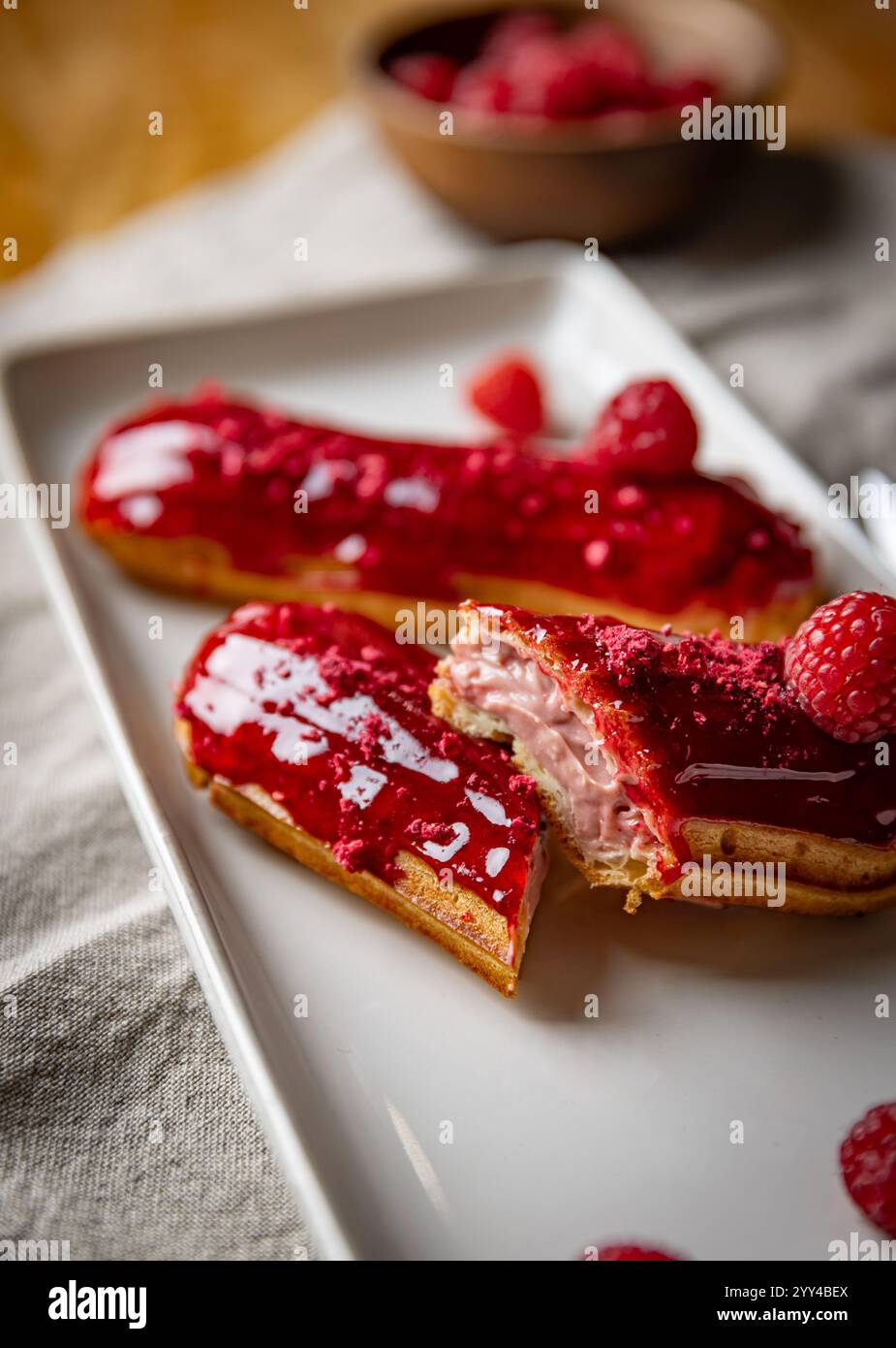 Raspberry eclairs with red raspberry icing resting on white rectangular plate Stock Photo