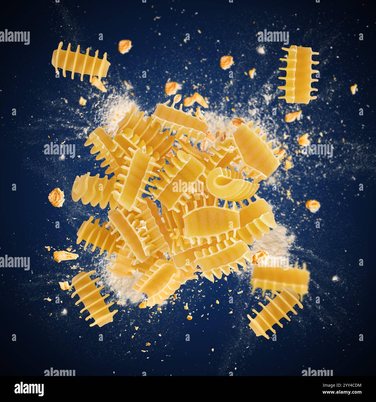 Radiatori pasta exploding with flour and whole wheat grains on blue background Stock Photo