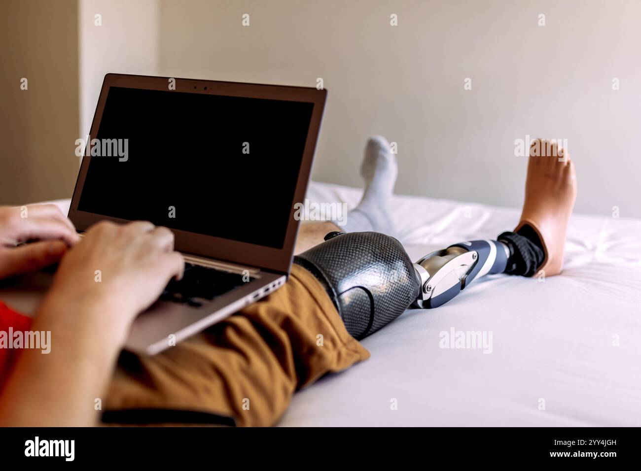 A man is sitting on a bed, using a laptop while wearing a high-tech ...