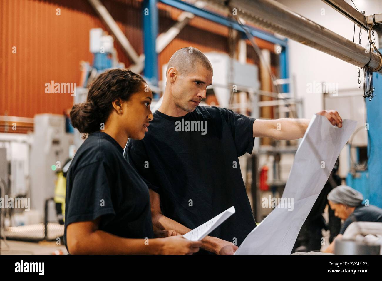 Mature man holding blueprint while standing next to female colleague in warehouse Stock Photo