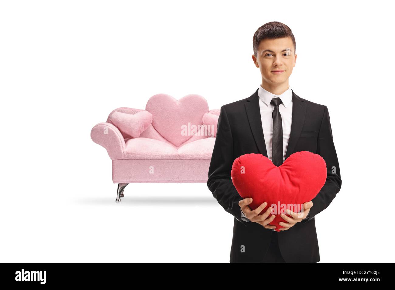 Young handsome man in a suit holding a red heart in front of a pink sofa isolated on white background Stock Photo
