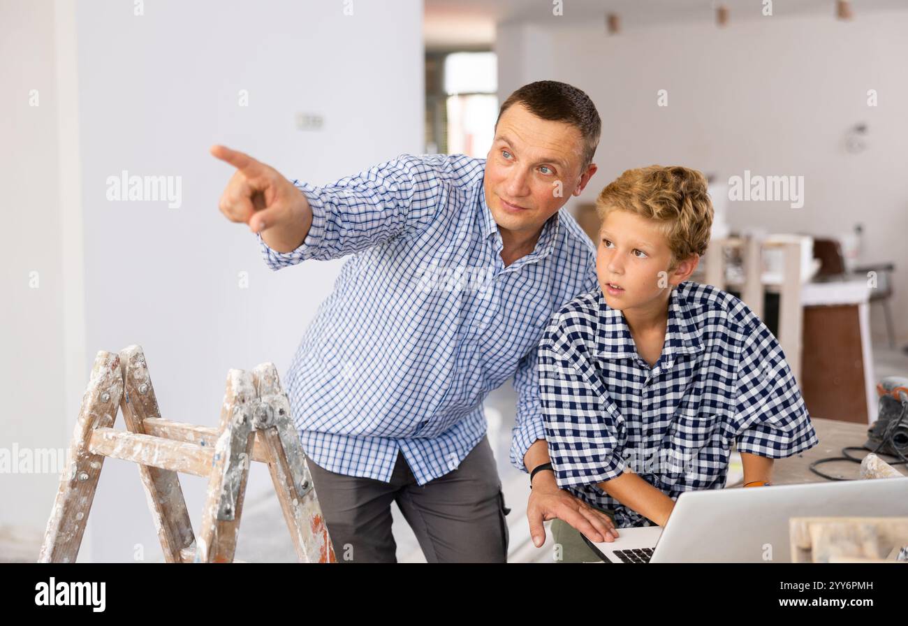 Man architect and boy using laptop while discussing working process in house being renovated Stock Photo