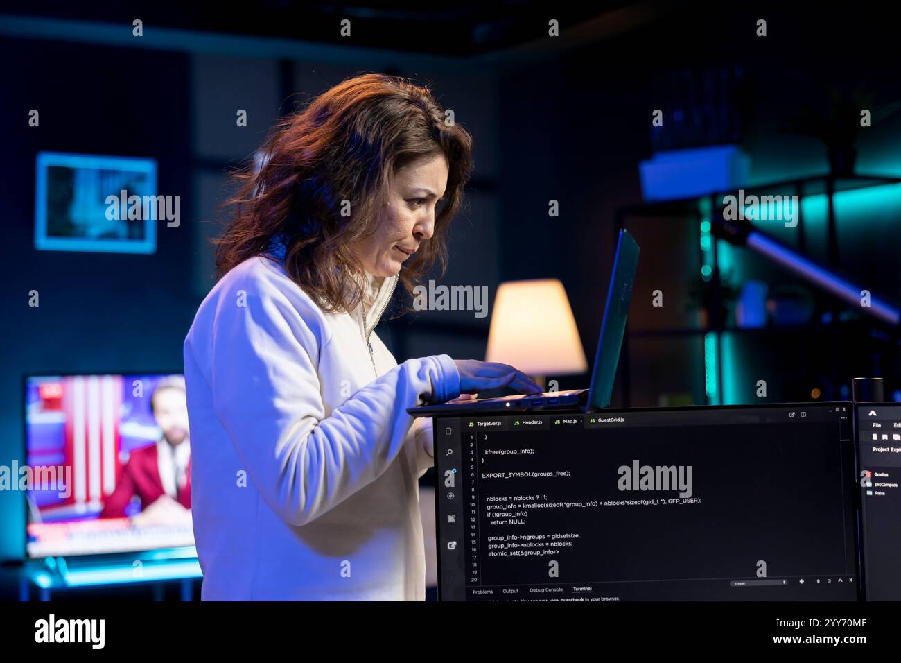IT specialist working from neon lit home using laptop, testing and deploying programs and systems. Software engineer checking code displayed on computer monitors, standing in apartment Stock Photo