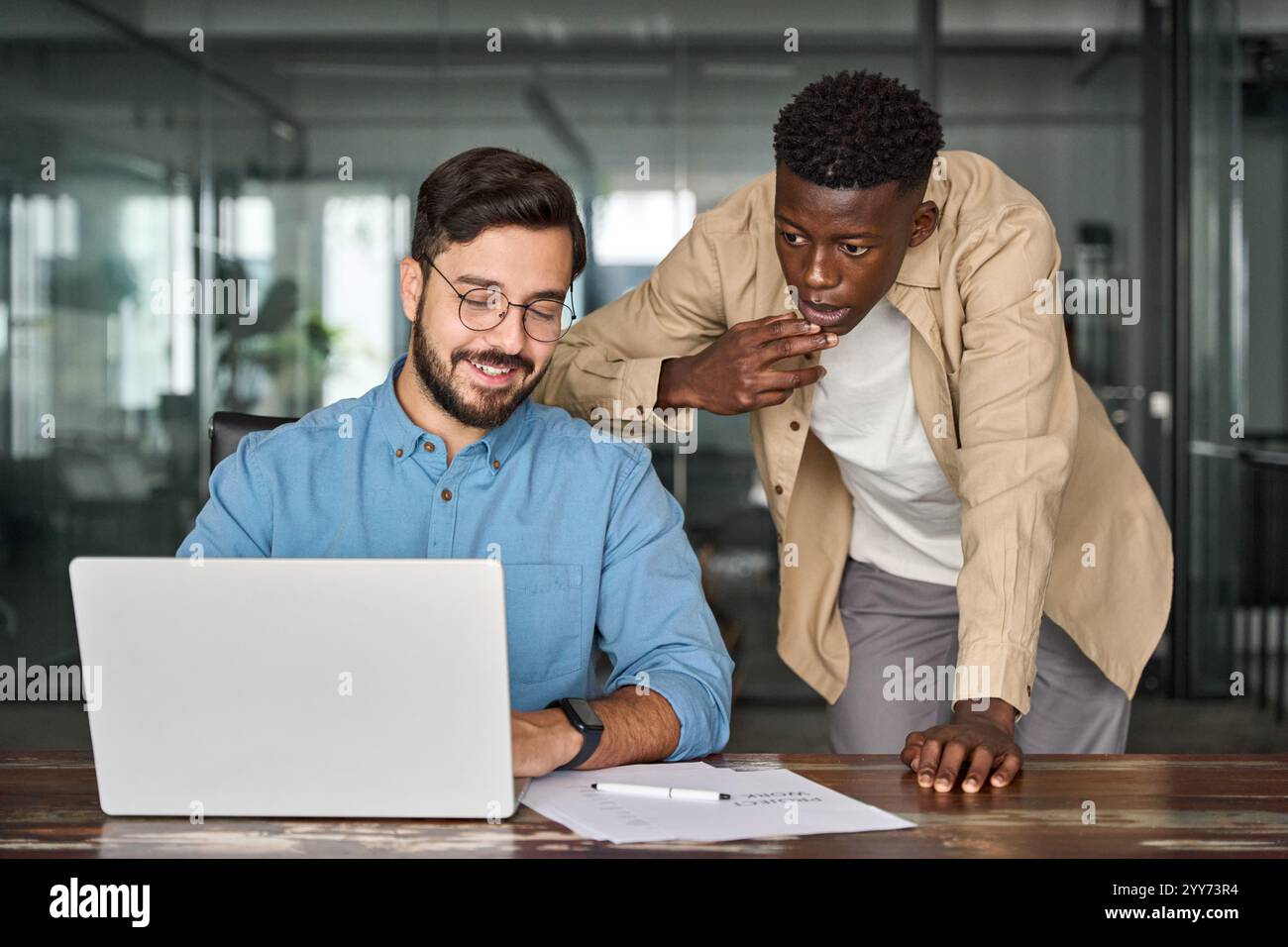 Two busy diverse professional coworkers discussing project working on laptop. Stock Photo