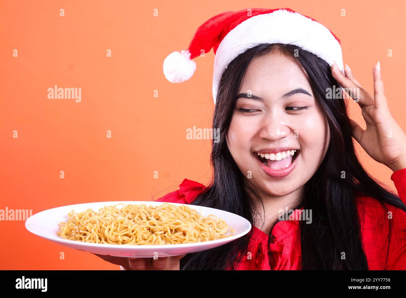 closeup gesture of beautiful women wearing red christmas blouse, Santa hat, cheerful to noodles, hand holding white plate filled with noodles to the s Stock Photo