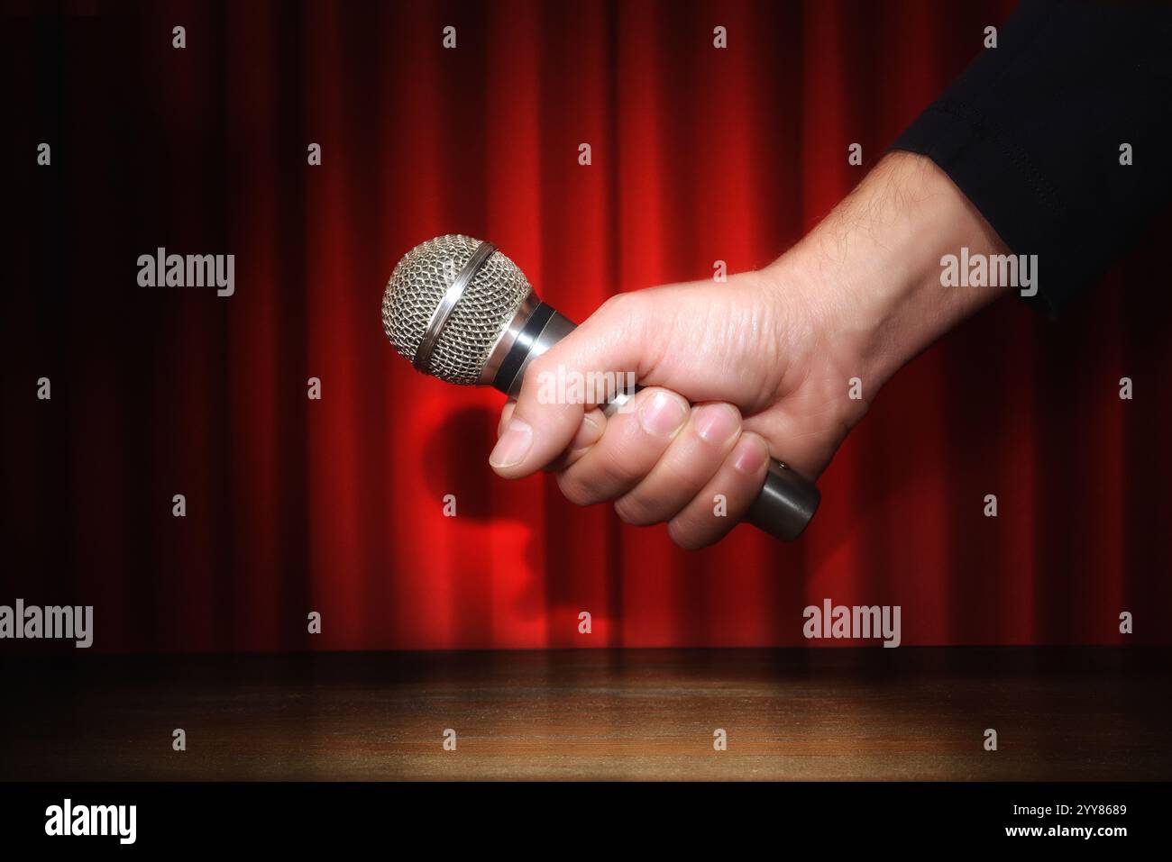 Hand holding a handheld microphone on a stage with red curtains ...