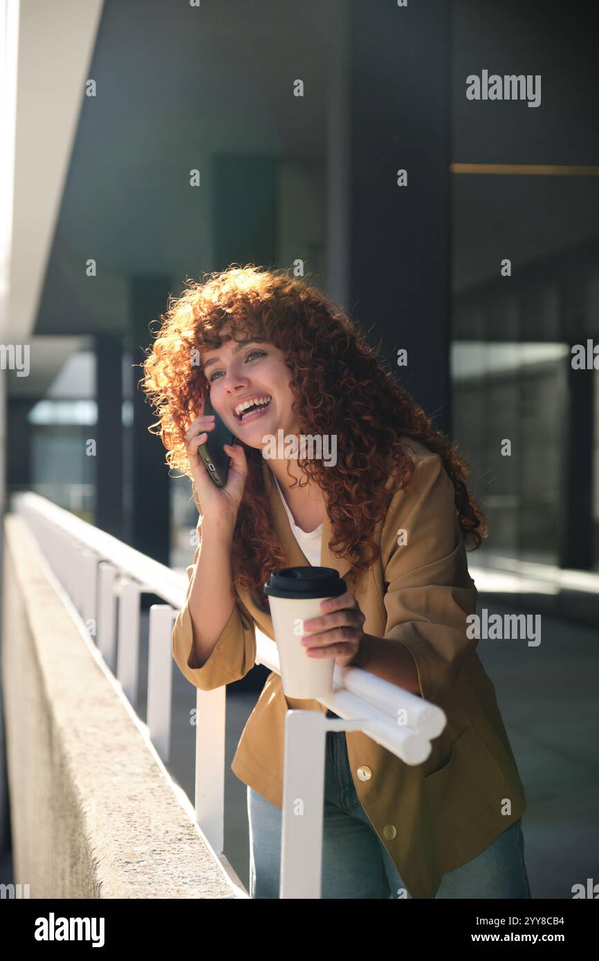 Happy businesswoman talking on phone and drinking coffee during break Stock Photo