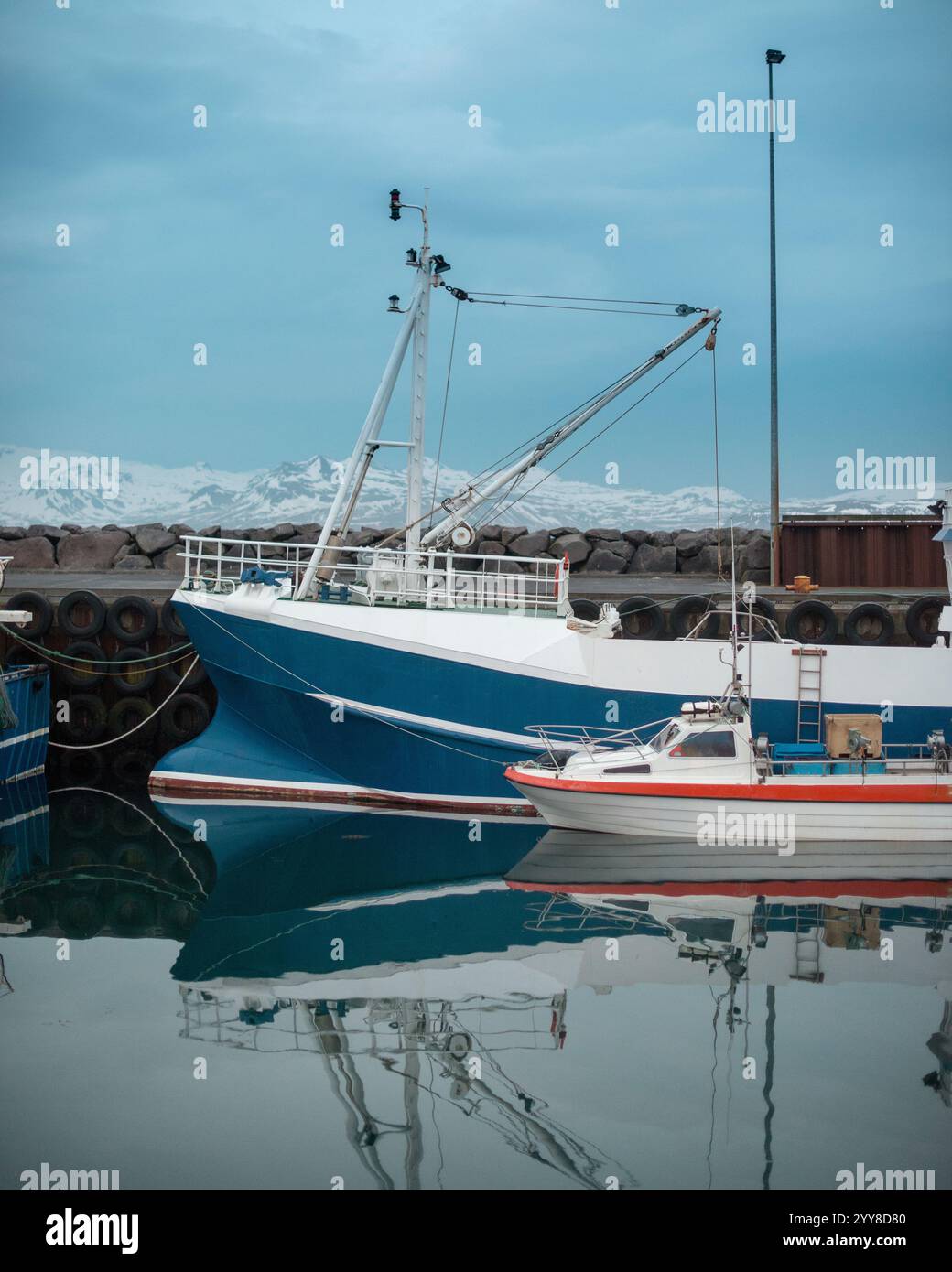 A tranquil scene of a white and blue boat reflected in the still water ...