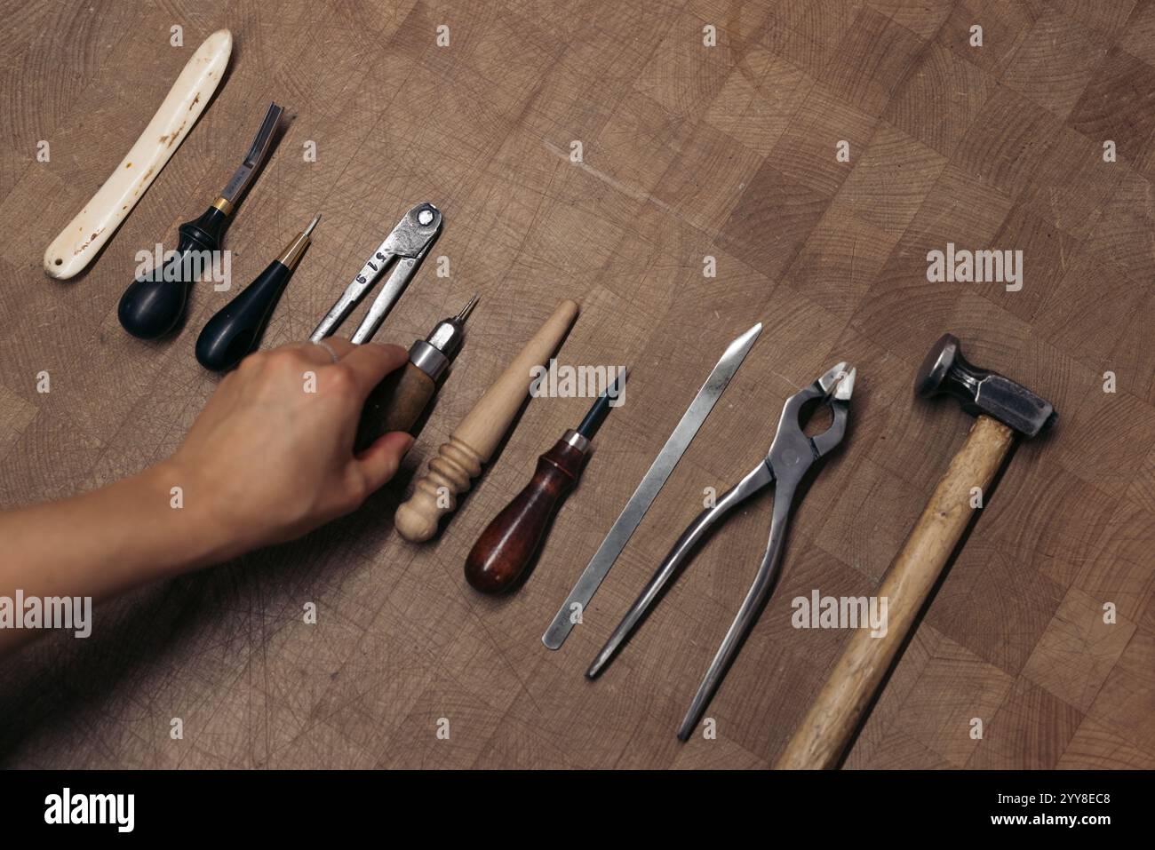 Artisan hand organizing leatherworking tools on wooden table Stock Photo
