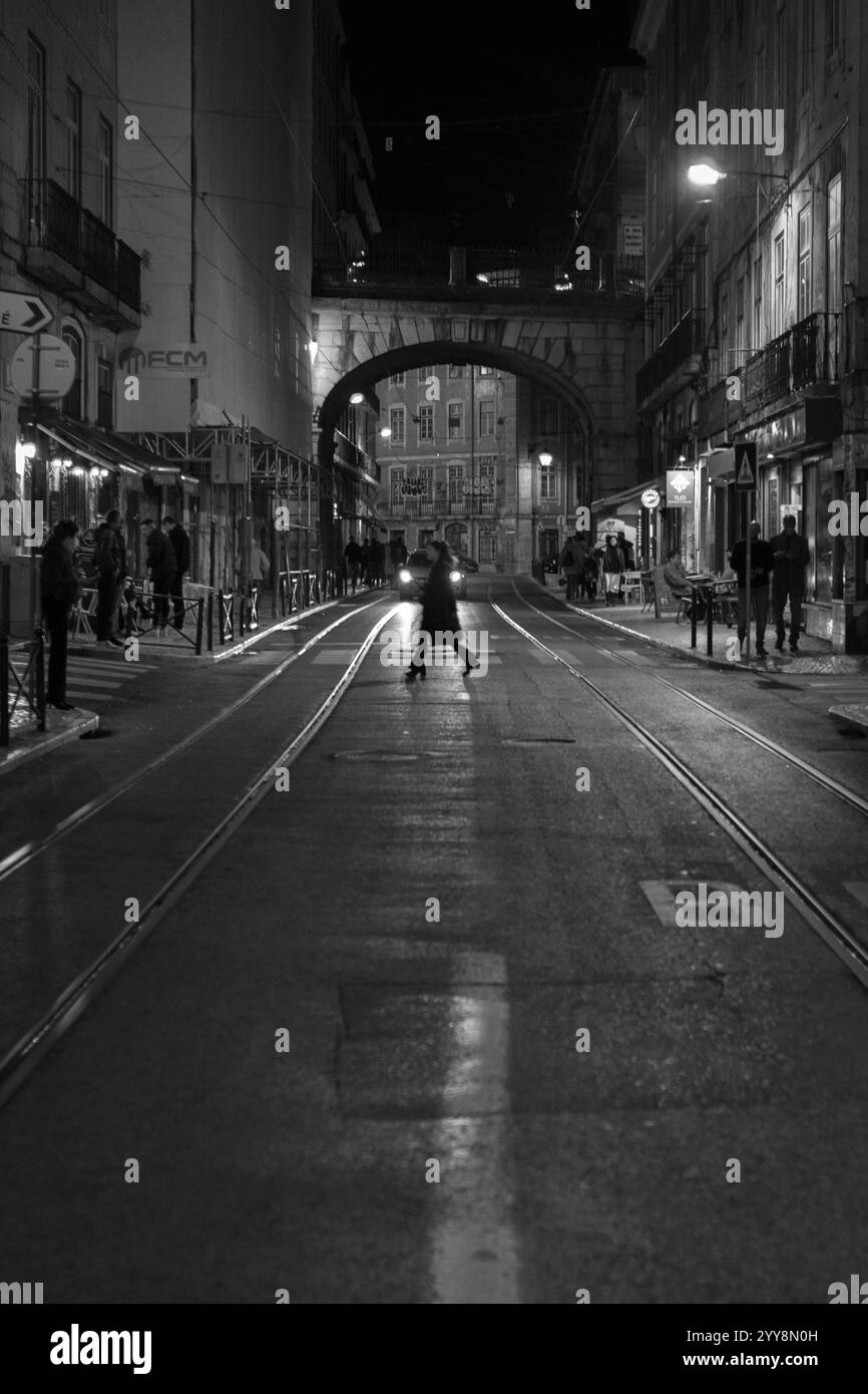 A person crossing a quiet street at night in Lisbon, Portugal, with historic architecture in the background Stock Photo