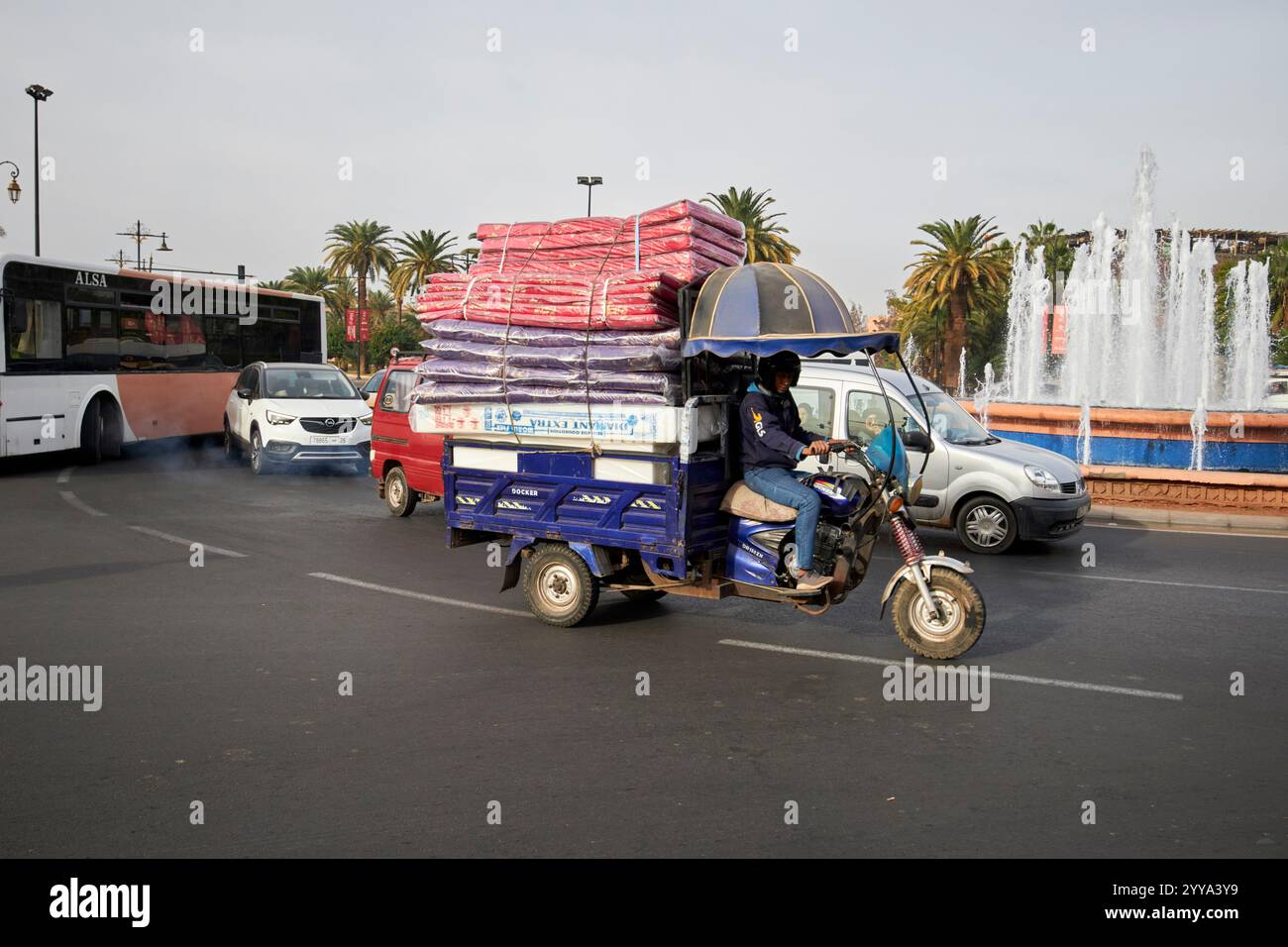 man driving tricycle motorbike to make deliveries in the old town at roundabout fountain in the road place bab jdid one of the old town gates marrakes Stock Photo