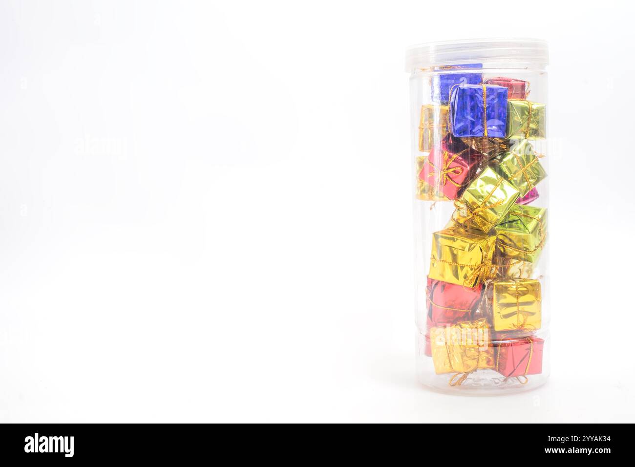 A pile of small, colorful gift boxes wrapped in shiny paper and arranged in a clear container, set against a vibrant white background. Perfect for hol Stock Photo